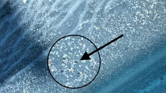 a zoomed in look at pool plaster with white rings around pebbles, indicating the loss of calcium hydroxide. This turns a dark pool grayish white.