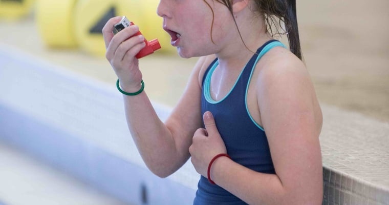 a girl with asthma using an inhaler to breathe in an indoor swimming pool with bad air quality from chloramines